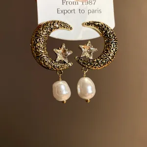 Detailed macro shot of vintage gold crescent moon and star earrings with baroque pearl drops