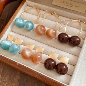 Detail view of colorful resin ball earrings and gold hoops in a wood jewelry box