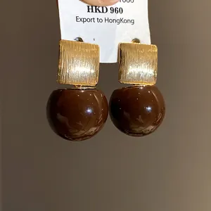 Detailed view of golden textured rectangular studs with glossy brown resin drops.