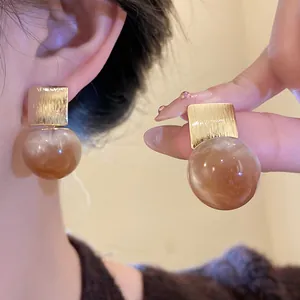 Close-up of golden square metal and amber marbled resin ball stud earrings on ear