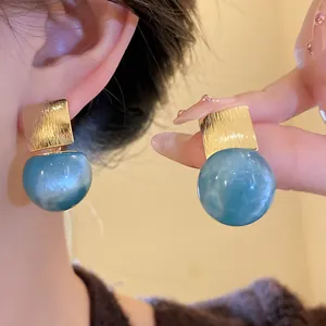 Macro view of blue marbled resin ball earrings with a textured gold square stud