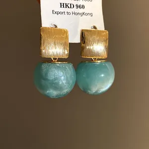 Detailed view of gold square stud earrings with shimmering teal resin beads