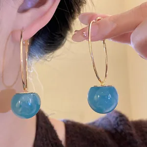 Detail shot of large gold hoop earrings with translucent blue resin candy drops.