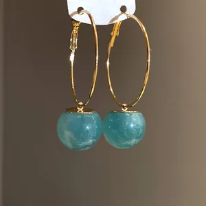 Detailed close-up of gold hoop earrings featuring vibrant turquoise resin ball charms.