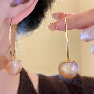 Detail view of gold hoop earrings with pearlescent resin sphere pendants on a model's ear