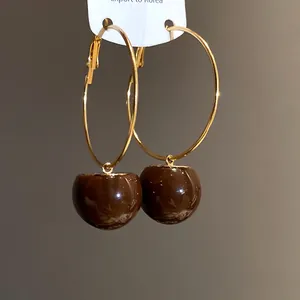 Detail of gold hoop earrings featuring glossy brown resin cherry pendants