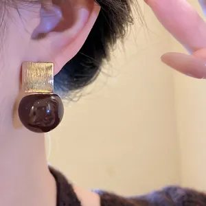 Detail of dark brown resin bead earring with gold textured square stud on ear