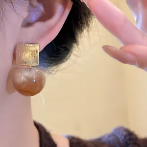 Close-up of elegant gold square and brown marble resin ball earrings on a model's ear