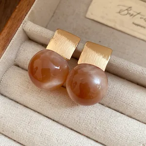 Detailed macro view of elegant gold and amber resin ball stud earrings in a jewelry box