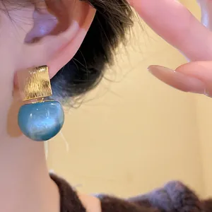 Macro detail shot of candy colored sky blue resin drop earrings with brushed gold finish