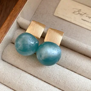 Close-up detail of candy-colored teal resin ball earrings with brushed gold squares