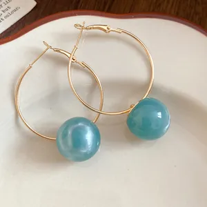 Close-up view of gold-tone hoop earrings featuring smooth teal resin spherical beads.