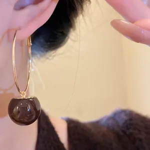 Detail view of a sweet candy-colored resin ball charm hanging on gold hoop earrings