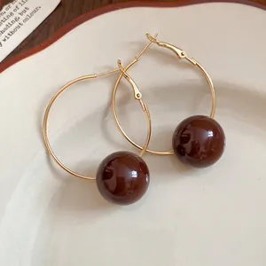 Close-up of brown resin ball hoop earrings on a decorative ceramic plate