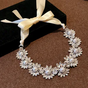 Detail view of flower-shaped crystal and pearl necklace with a cream silk ribbon tie