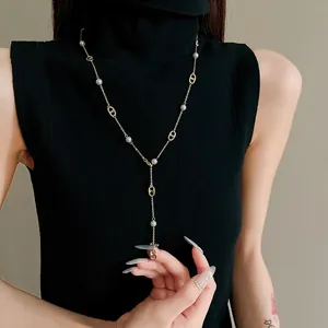 Close-up of gold-plated pig nose and pearl long Y-shaped necklace on black turtleneck