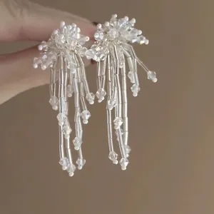 Primer plano de pendientes hechos a mano con flores de cuentas blancas y borlas finas