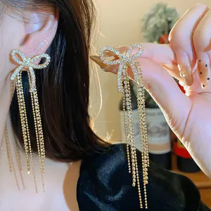 Detail shot of elegant zircon bow earrings with long gold tassels on a model's ear