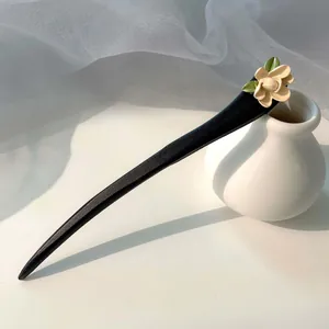 Vista dettagliata di un elegante fermaglio per capelli nero con fiore crema e foglie