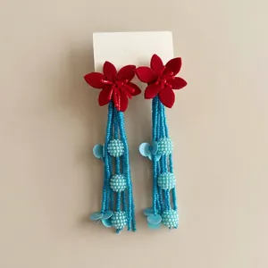 Detalle de pendientes de flores rojas con borlas de cuentas azules y lentejuelas