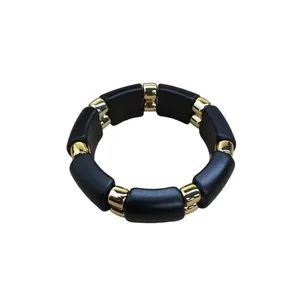 Elegante pulsera elástica de acrílico negro con espaciadores dorados sobre fondo blanco