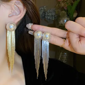 Close-up detail of long metallic tassel earrings in gold and silver worn by model