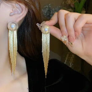 Detailed close-up of elegant long gold tassel earrings with large pearls on a model