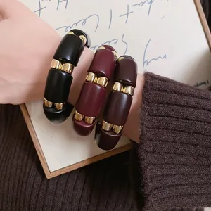 Primer plano de tres pulseras de acrílico con separadores de metal dorado en la muñeca.