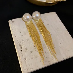 Detailed view of elegant gold tassel earrings with white pearls on a textured stone slab