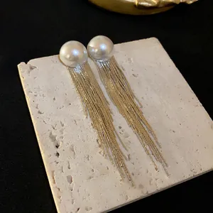 Detailed shot of elegant long gold tassel earrings with white pearls on a stone base