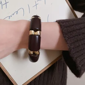 Vista detallada de una pulsera de acrílico marrón oscuro con piezas doradas en la muñeca