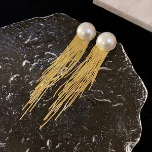 Close-up of elegant gold tassel earrings featuring large white half-pearl studs and chains