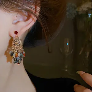 Elegant gold-tone flower crystal tassel drop earrings worn on ear in warm lighting