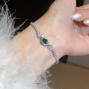 Dettaglio dell'elegante bracciale in zircone verde ovale sul polso con piume.