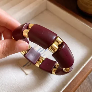 Primer plano detallado que muestra los segmentos de acrílico granate y metal dorado de la pulsera.