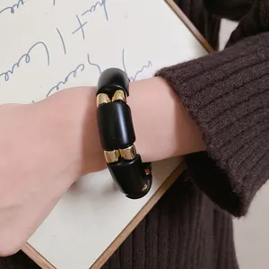 Primer plano de una pulsera minimalista de acrílico negro y dorado en una muñeca.