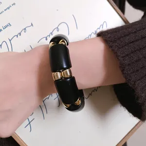 Primer plano de una pulsera minimalista de acrílico negro y cuentas doradas en la muñeca.