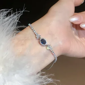 Dettaglio di un elegante bracciale in zircone blu ovale al polso con piume bianche