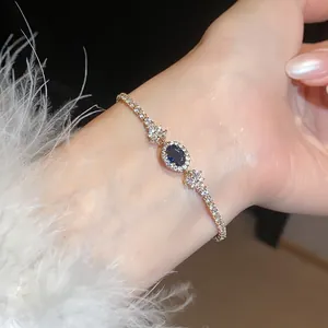 Primo piano di un elegante bracciale dorato con una pietra di zirconia blu ovale.