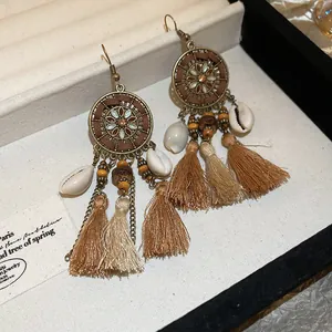 Dettaglio di orecchini boho con nappe, conchiglie, perline in legno e ciondoli fiore.