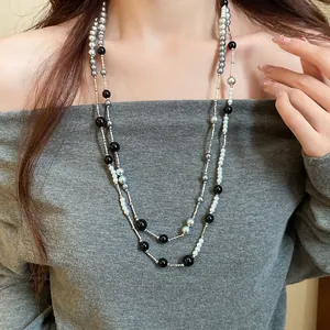 Close-up of a double-layer long necklace with black, grey, and pearl beads on a model