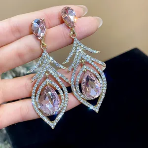Close-up of pink teardrop crystal feather earrings with sparkling micro-pave diamonds.