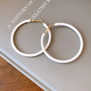 Close-up detail of white leather wrapped round hoop earrings with golden minimalist accents