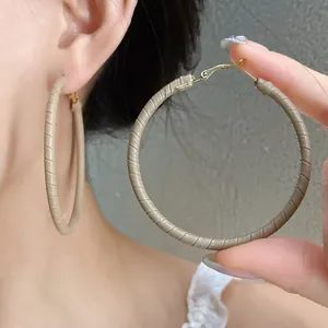 Detailed macro shot of leather-wrapped beige hoop earrings shown on ear for size reference