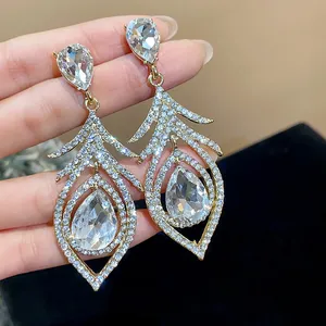 Close-up detail of luxurious crystal encrusted hollow feather drop earrings held by hand