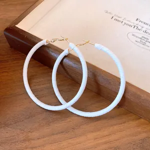 Close-up detail of stylish large white leather wrapped hoop earrings on a wooden tray