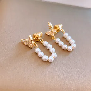 Primer plano de pendientes de mariposa bañados en oro con circonitas y perlas