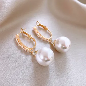 Detalle de elegantes pendientes largos bañados en oro con circonitas y perlas blancas