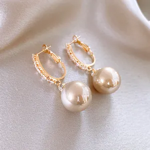 Vista detallada de pendientes de aro dorados con circonitas y perlas color champán