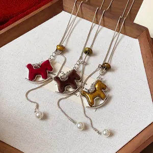Nahaufnahme von beflockten Schaukelpferd-Halsketten in Rot, Braun und Gold mit Perlen.